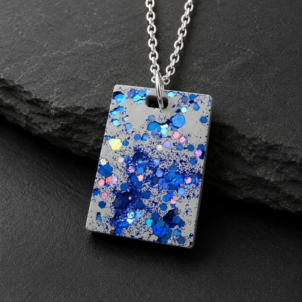 Gray rectangular pendant necklace with blue glitter hexagons on a silver chain, set against a dark background; jewelry product photo.