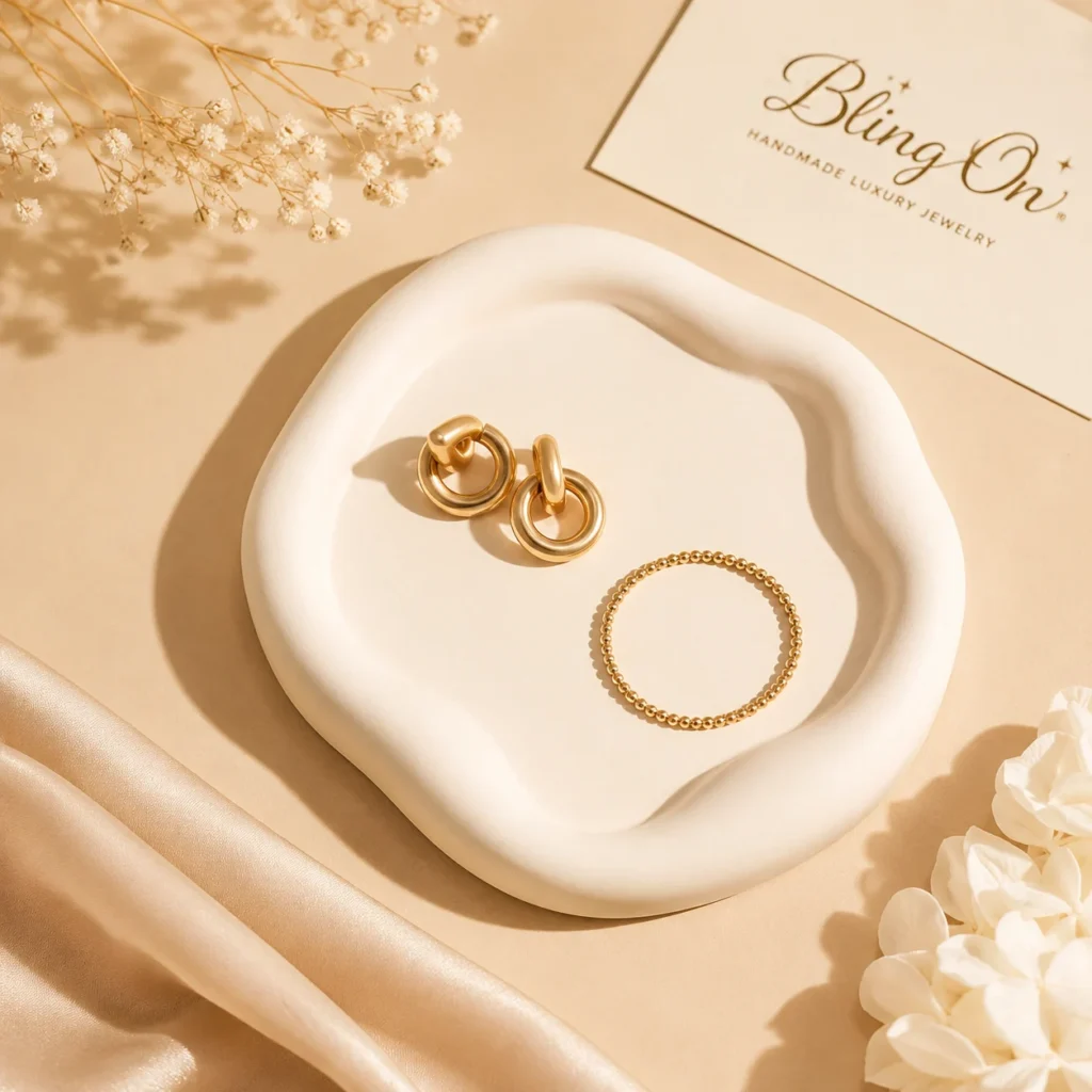 Golden hoop earrings and a beaded ring placed on a white ceramic plate with a Bling On card in soft beige tones, jewelry on display.