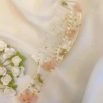 Handmade floral resin hair comb with handle featuring pink flowers and gold flakes on soft satin background
