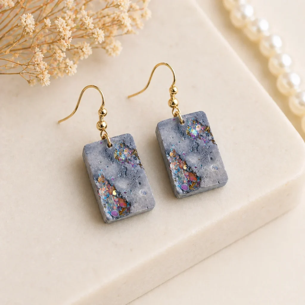 Rectangular Gray Resin Earrings with Iridescent Confetti Inlays on Gold Hooks Shown on a Light Stone Surface with Dried Flowers Nearby  Bling On