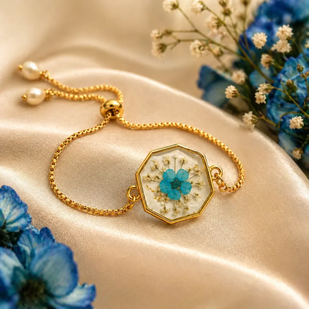 Gold octagonal pendant bracelet with a preserved blue flower centerpiece on satin fabric backdrop.