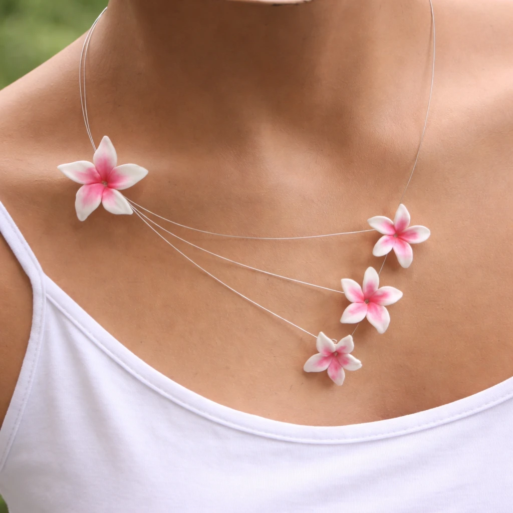 Delicate silver necklace with four pink‑white plumeria flowers draped across the collarbone area. Polymer clay jewellery