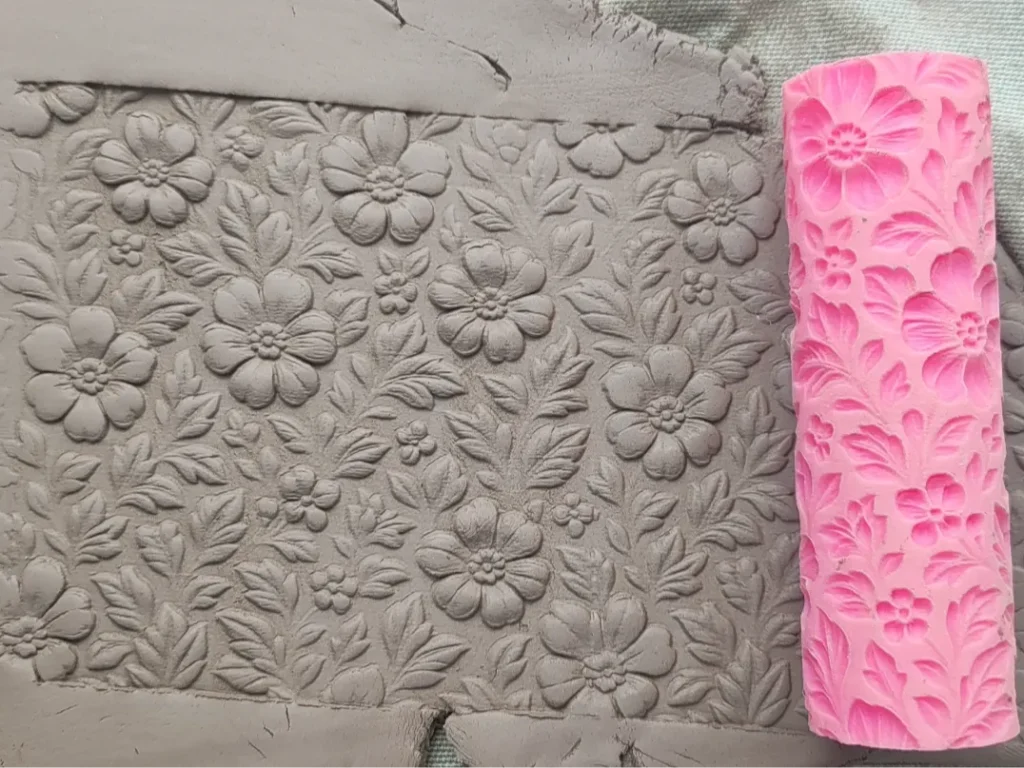 Grey clay slab embossed with a dense floral pattern of large flowers and leaves for texture.