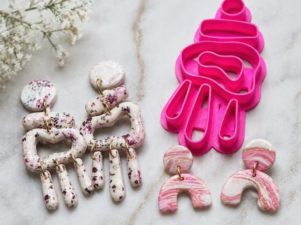 Polymer clay cutter set with abstract drip design in bright pink, displayed beside handmade marbled polymer clay earrings with gold accents on a light textured background, ideal for jewellery making and DIY craft tools.