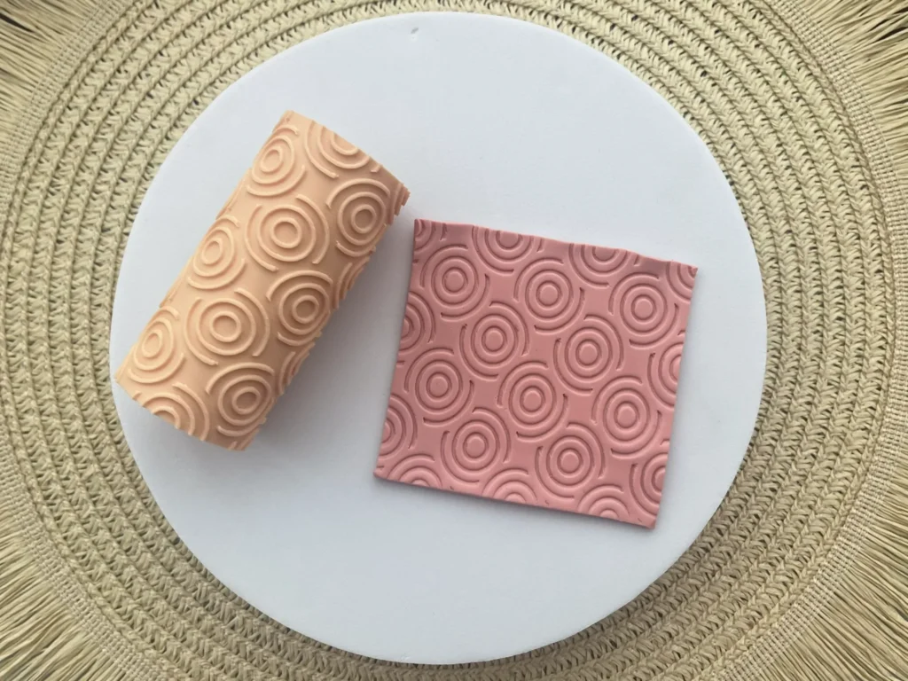 Two decorative soaps with circular swirl patterns sit on a white plate atop a woven mat (peach and pink tones).