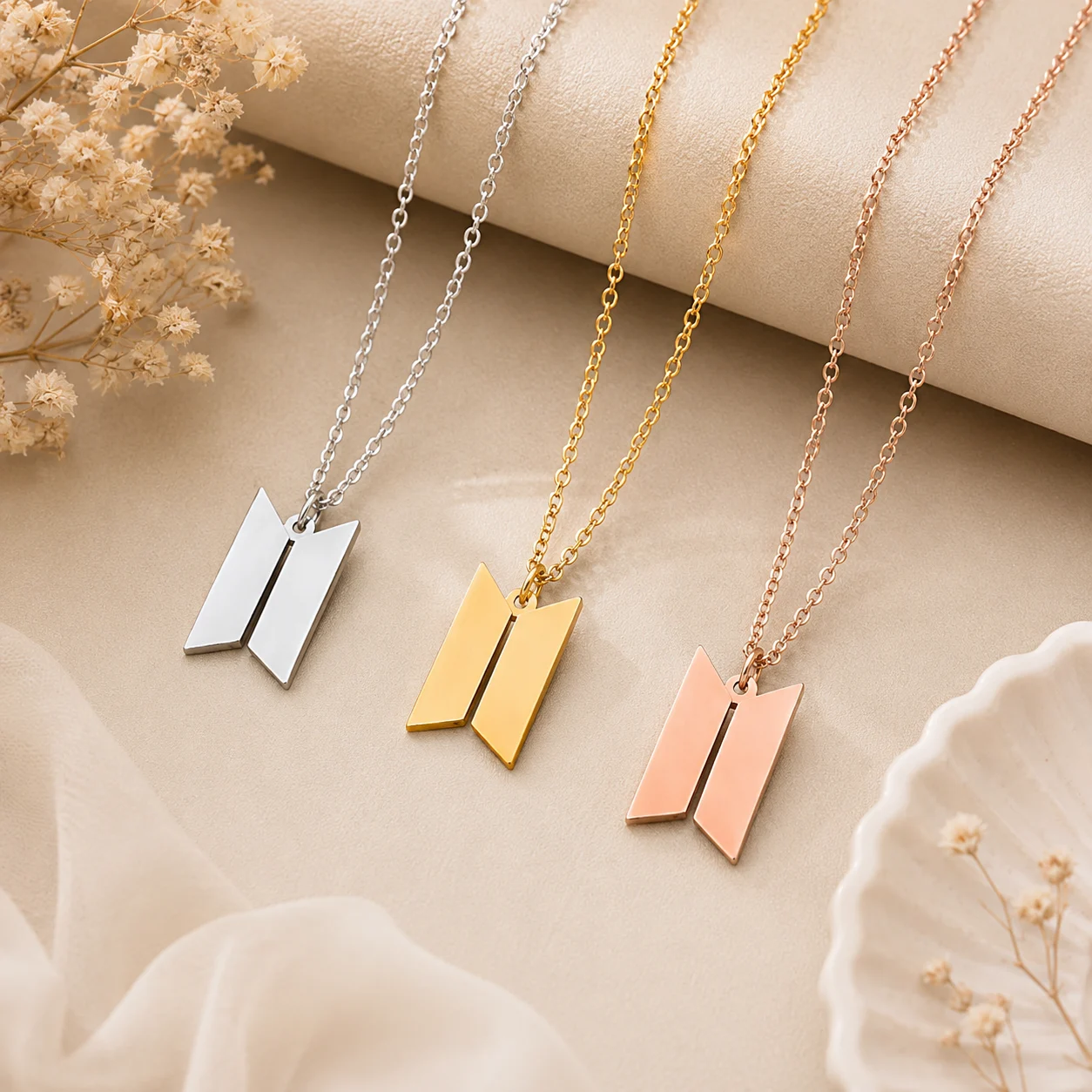 Three V-shaped pendant necklaces in silver, gold, and rose gold on delicate chains laid on a beige background.