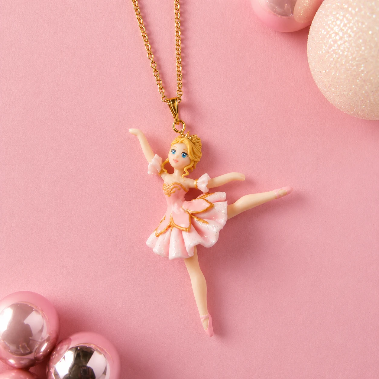 Gold chain necklace with a pink ballerina pendant in a tutu on a pink background.