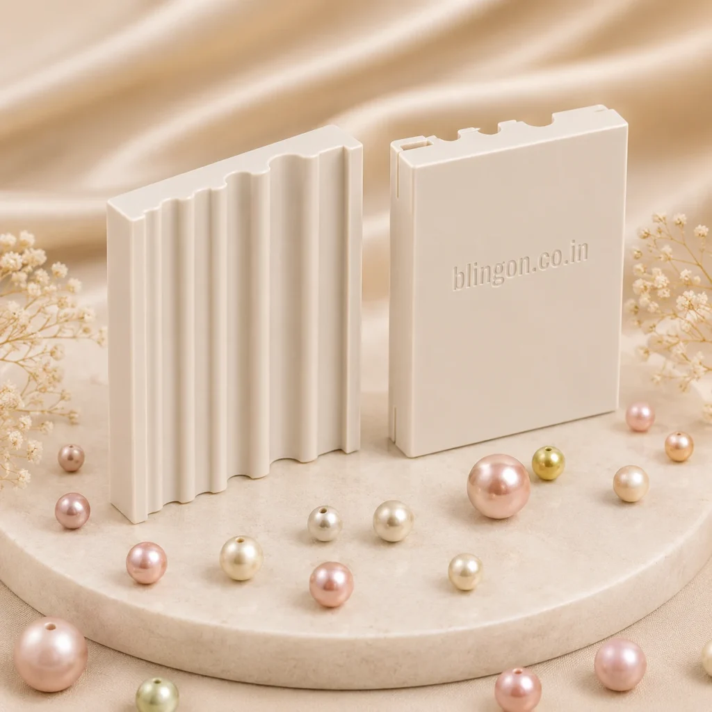 Two white plastic display blocks with vertical ridges on a beige pedestal, one showing the embossed 'blingon.co.in' text, surrounded by pastel beads.