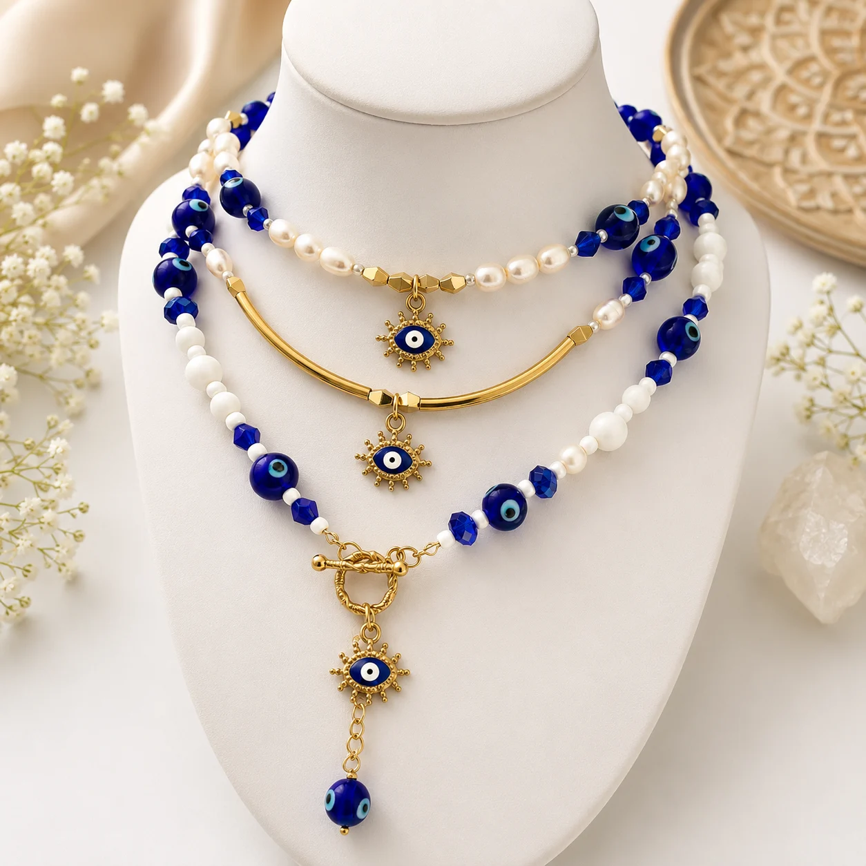 Layered blue and white bead necklace set with gold accents and hanging evil-eye charms on a display bust