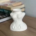 White Decorative Vase with Raised Scrollwork Pattern Sits on a Wooden Surface Blurred Books in the Background  Bling On
