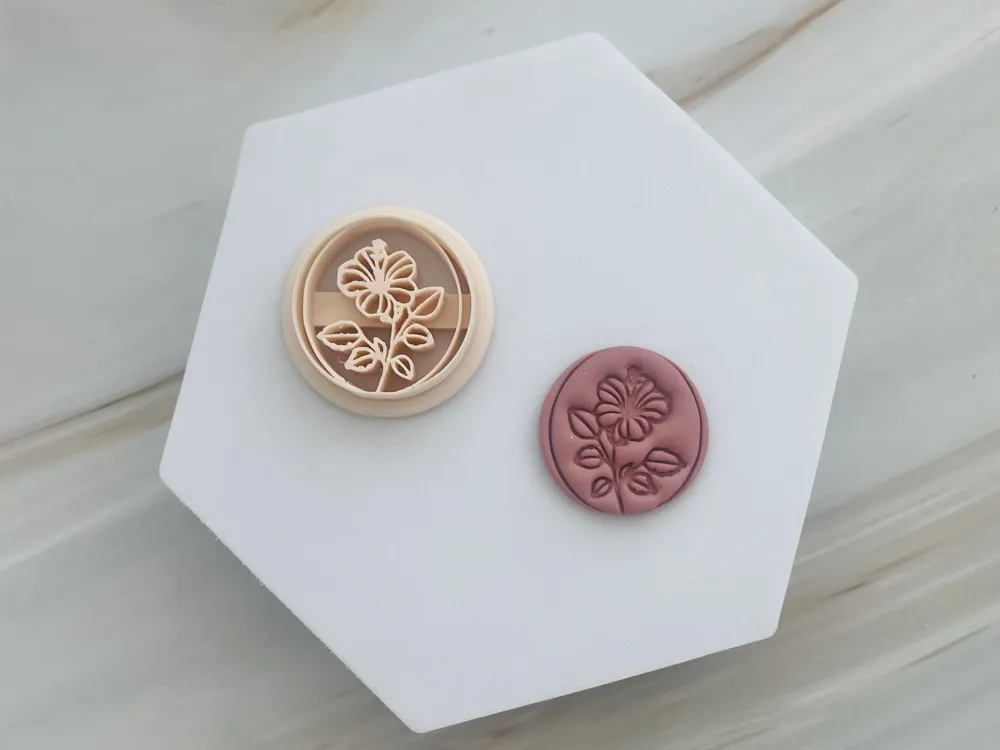 Two circular wax seals with embossed floral design on a white hexagonal tile, one beige and one dusty pink, resting on a marble surface.
