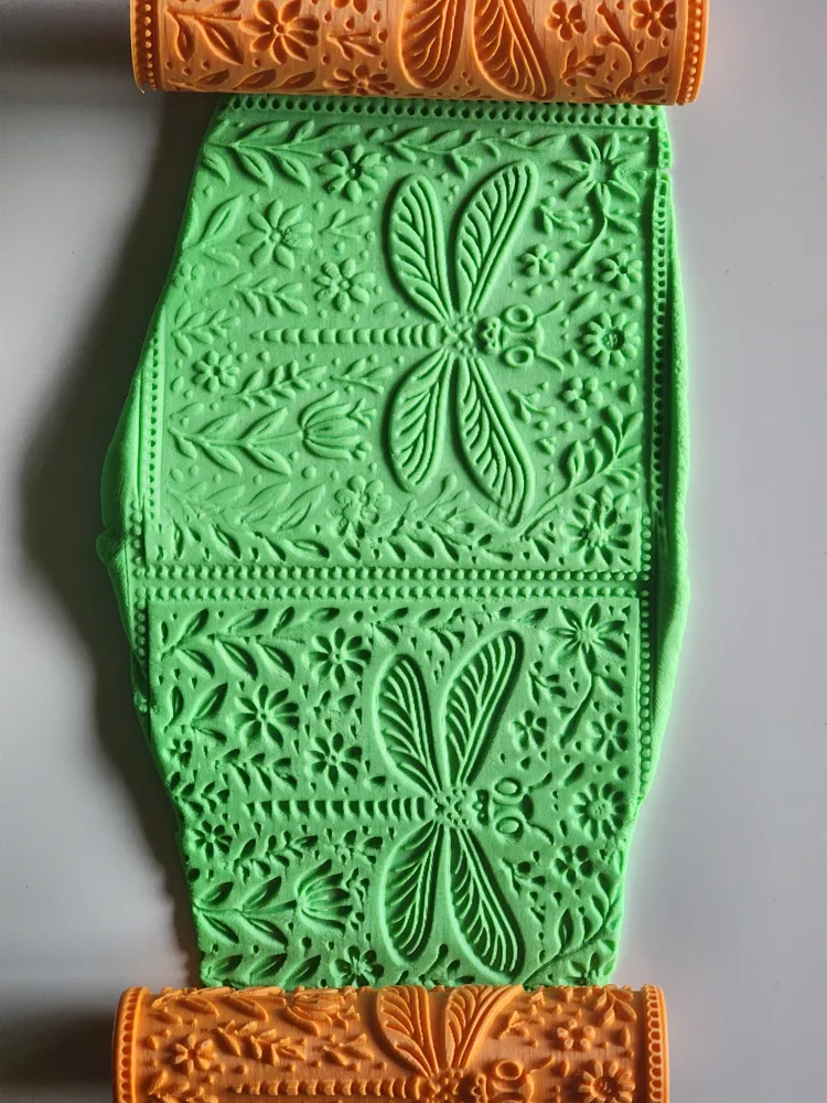 Green fondant embossed with dragonflies and flowers, shown with orange decorative embossing rollers at top and bottom.